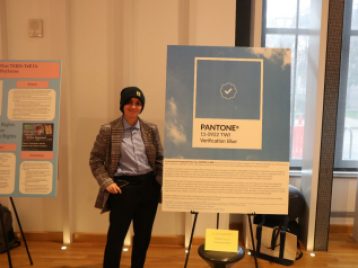 Eli Miller stands beside a large presentation board with their project, "Verification Blue."